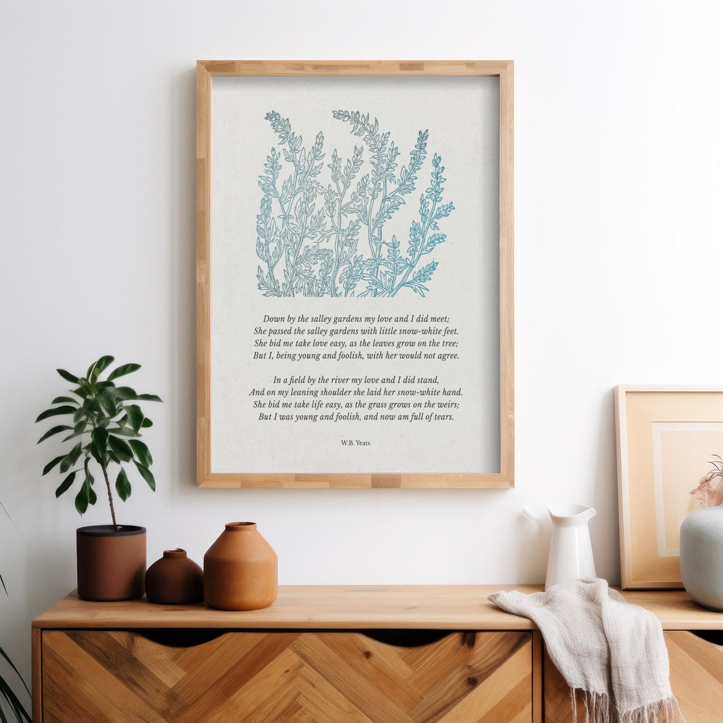 A modern minimalist space with the framed “Down by the Salley Gardens” print displayed above a wooden dresser, styled with earth-toned pottery and a green plant for a natural, peaceful touch.