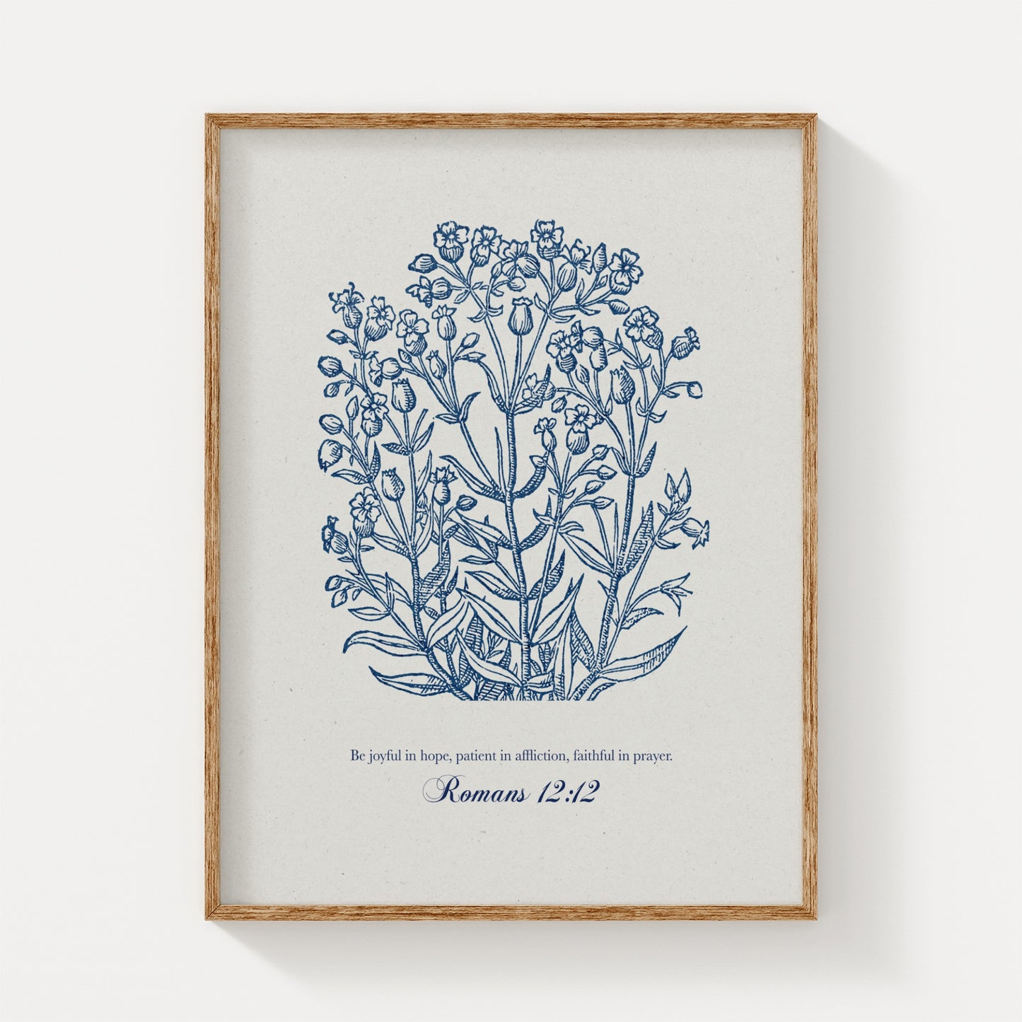 Botanical art print featuring delicate blue floral illustrations paired with the Bible verse Romans 12:12, displayed in a natural wood frame on a light background.
