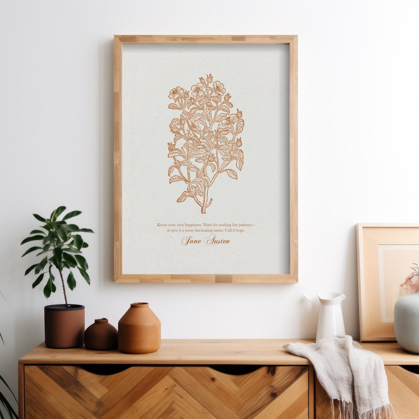 Botanical art print with warm golden floral details and a Jane Austen quote, framed in natural wood and styled on a wooden dresser with terracotta vases, a green plant, and neutral decor.