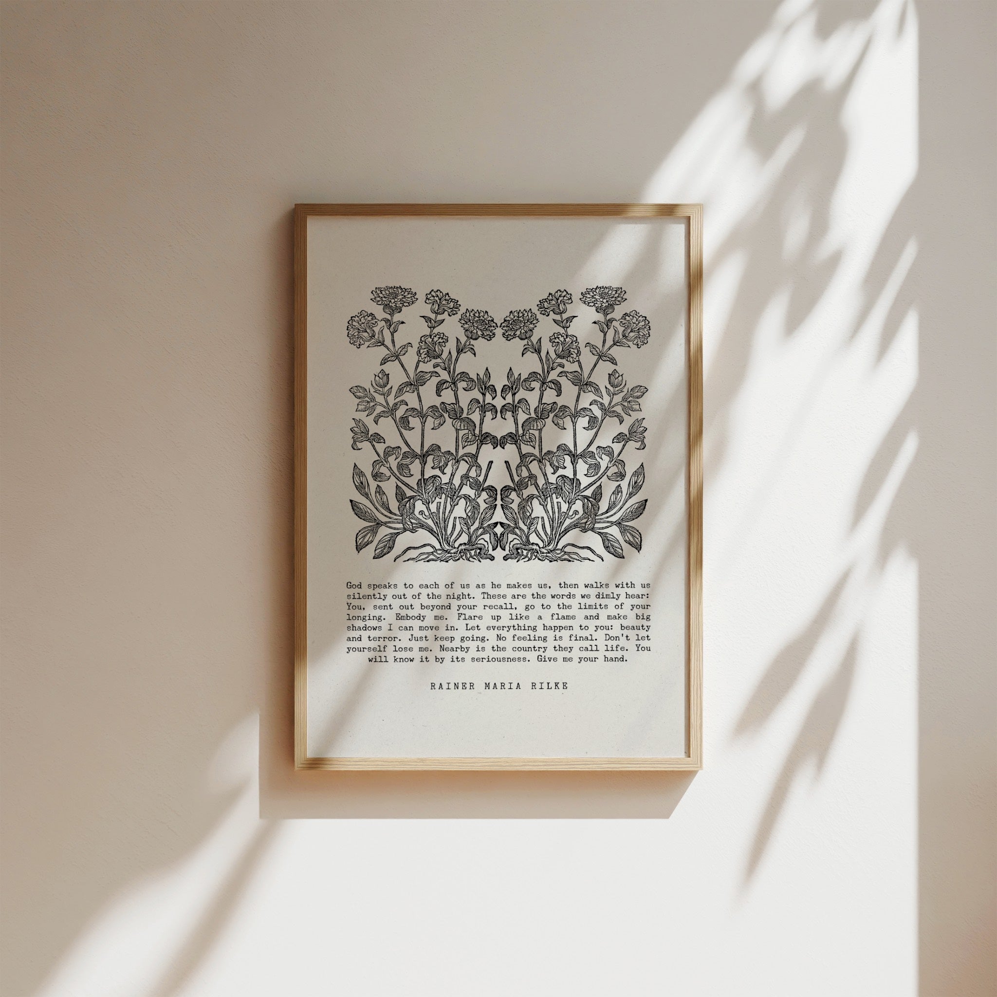 Botanical art print featuring a detailed black floral illustration paired with an excerpt from Rainer Maria Rilke’s writing, framed in natural wood and displayed on a white background  with soft shadows for a timeless and literary aesthetic.