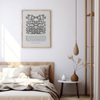 Art print with black floral designs and Rainer Maria Rilke’s text styled above a neutral bed with soft bedding and a minimalist bedside table featuring a modern vase and candle.