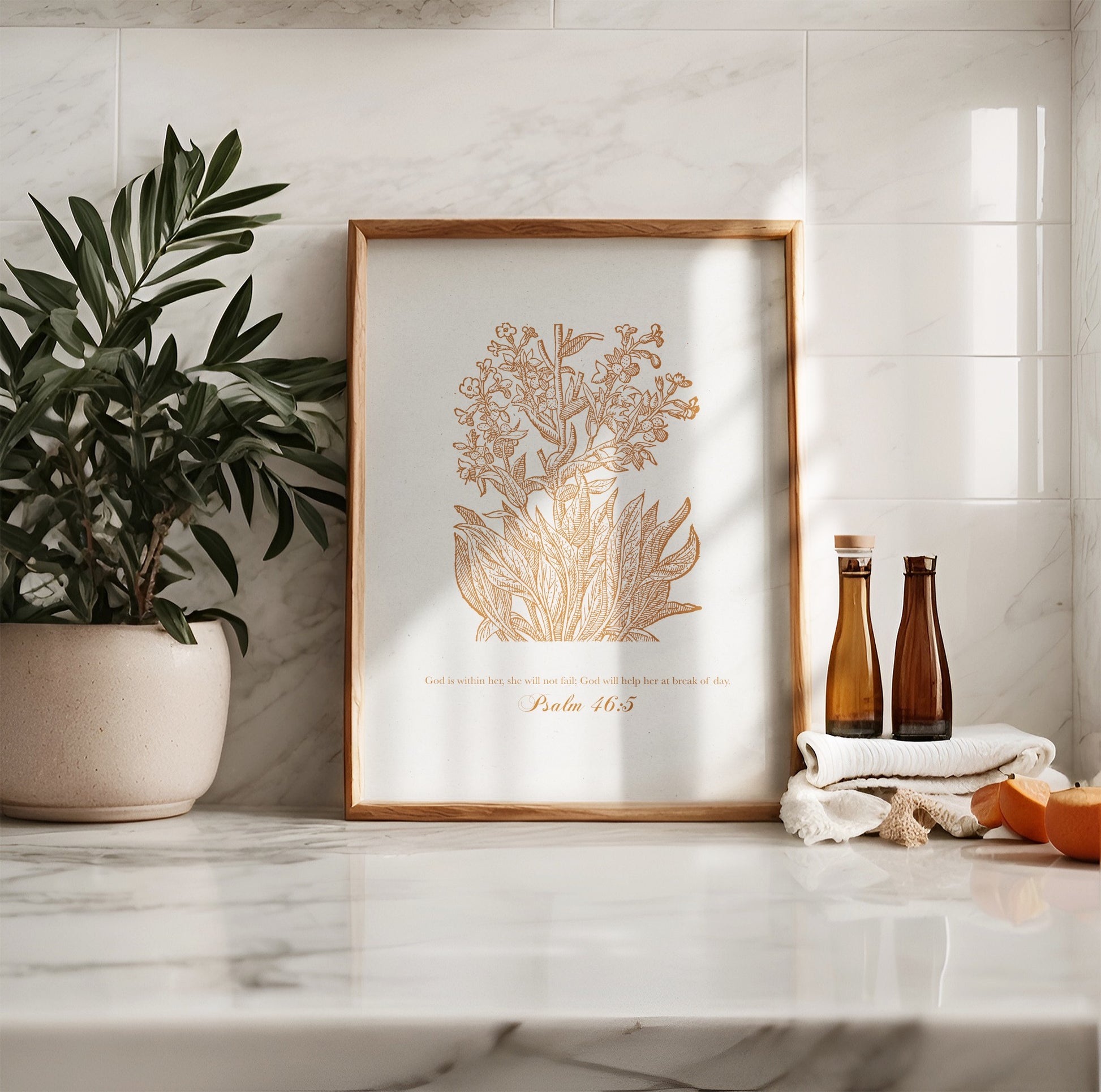 Golden floral botanical art print with Psalm 46:5, leaning on a marble countertop with decor elements like potted greenery and amber glass bottles.