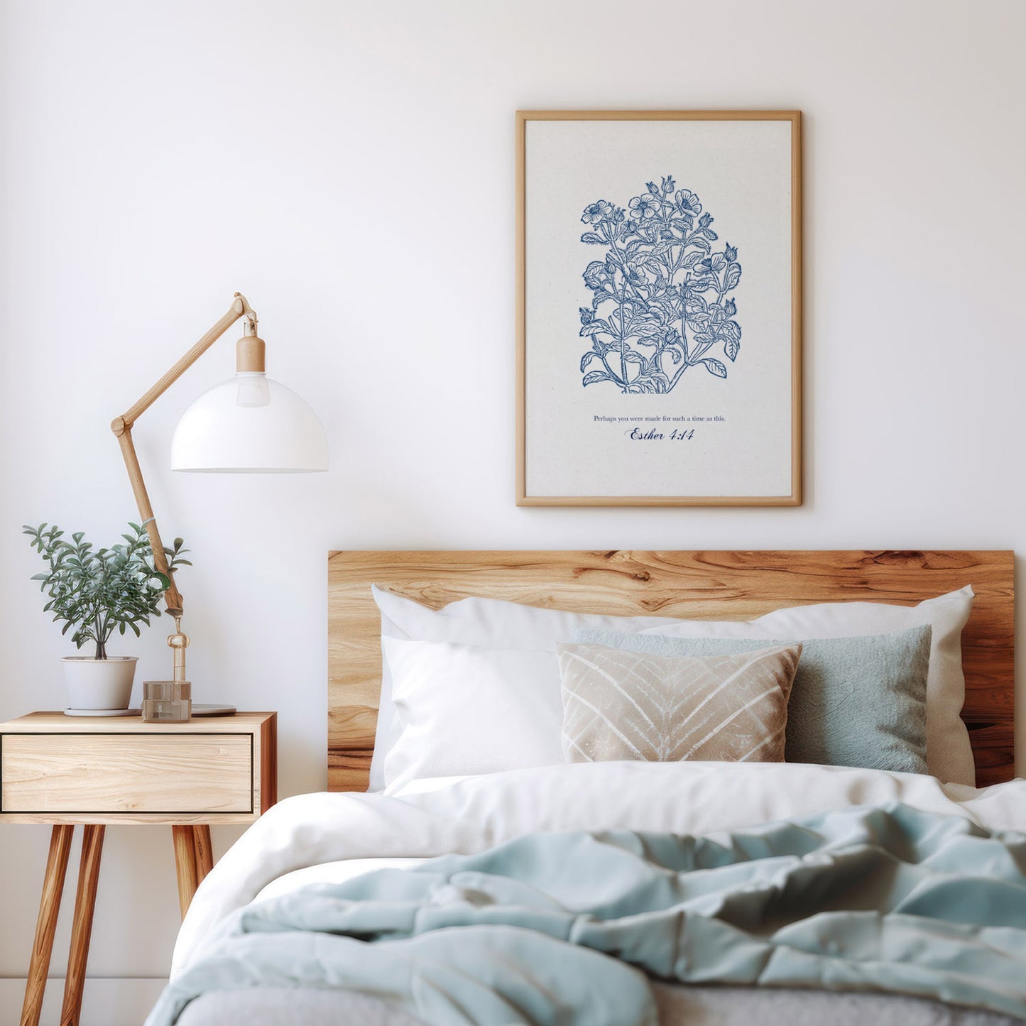 Art print with blue floral designs and Esther 4:14 styled above a cozy bed with neutral bedding, a wooden side table, and a minimalist lamp.