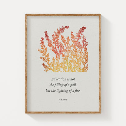 A framed art print featuring W.B. Yeats’ quote about education, elegantly paired with warm-toned botanical illustrations in shades of red and gold, displayed on a neutral background with a natural wood frame.