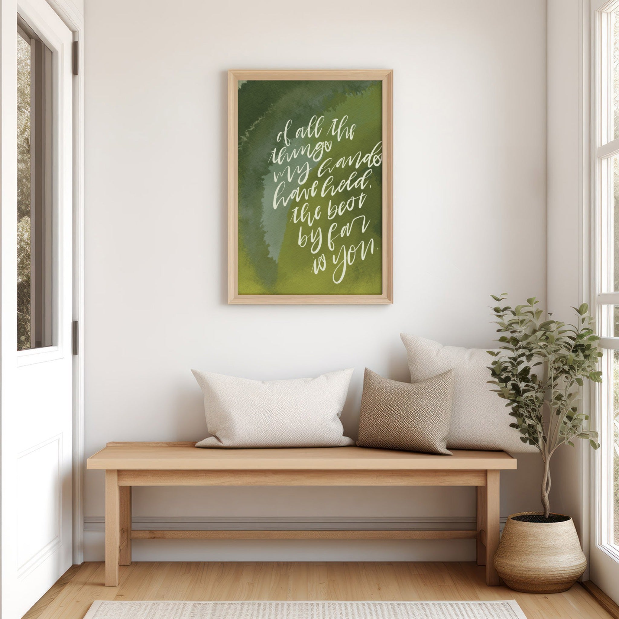Wooden bench with pillows against a wall with a framed handlettered quote print