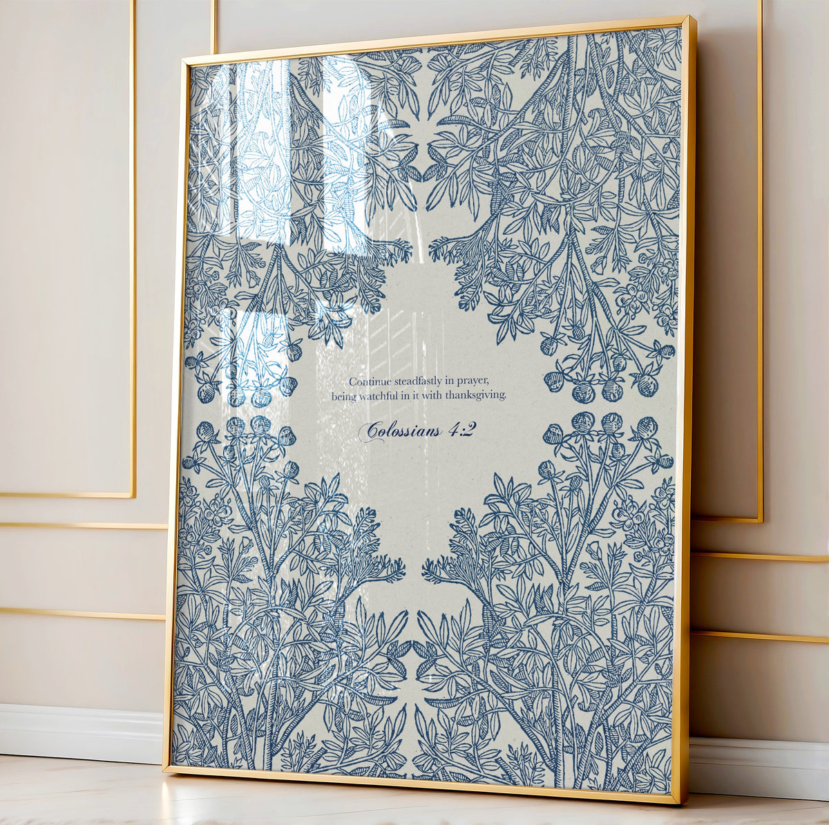 Close-up of the botanical art print featuring intricate blue floral patterns and Colossians 4:2, framed in natural wood and leaning against a paneled wall.