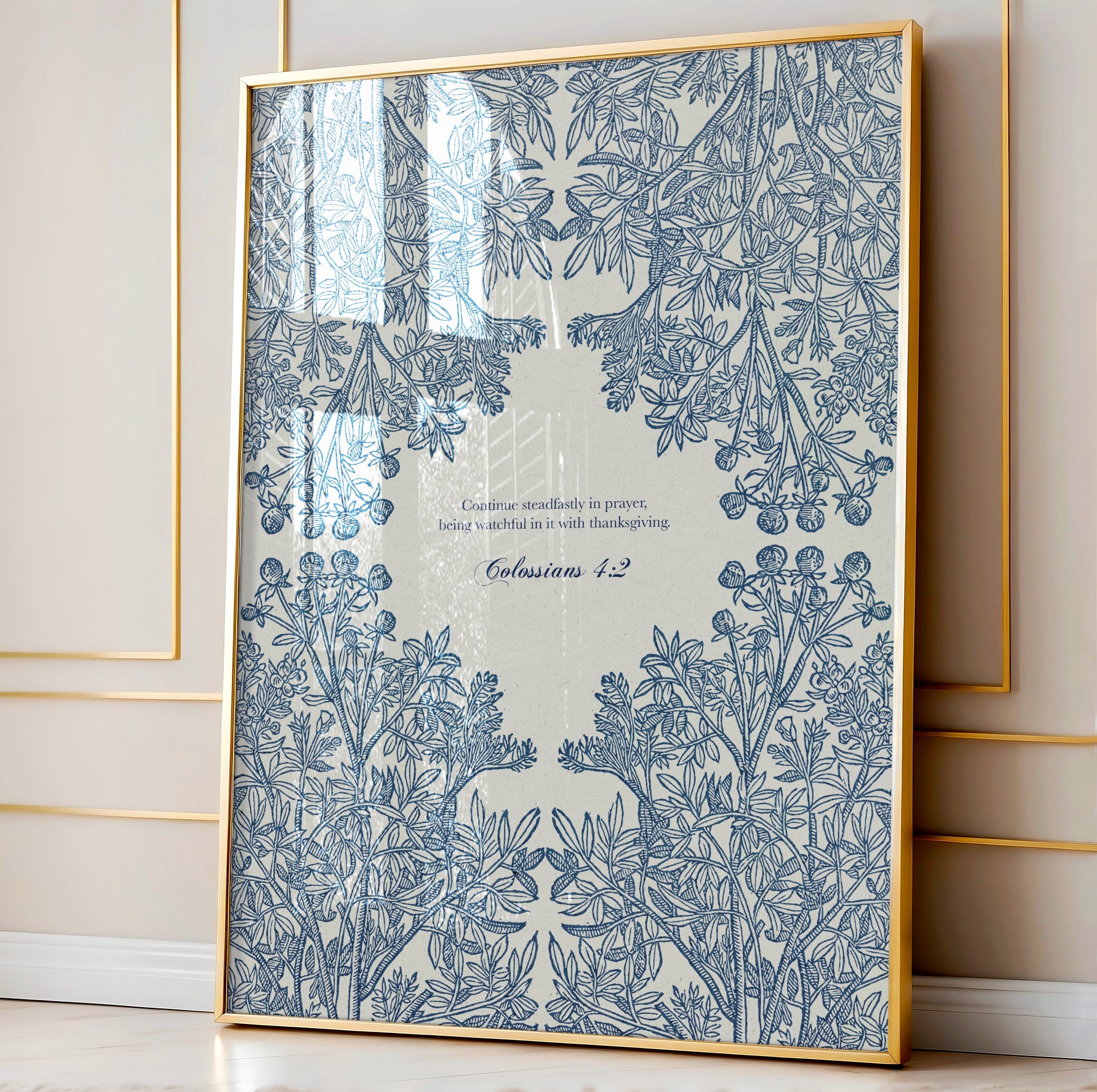 Close-up of the botanical art print featuring intricate blue floral patterns and Colossians 1:17, framed in natural wood and leaning against a paneled wall.