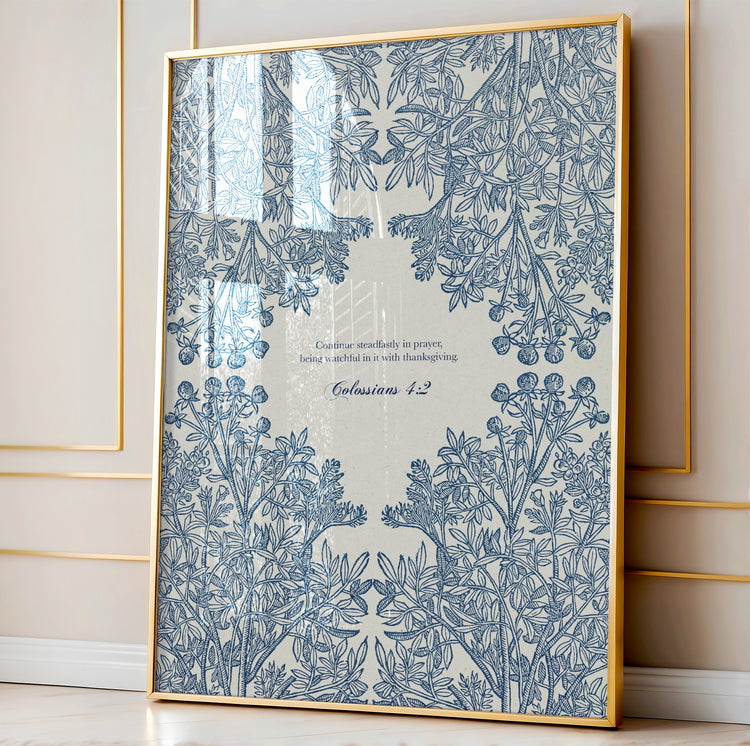 Close-up of the botanical art print featuring intricate blue floral patterns and Colossians 4:2, framed in natural wood and leaning against a paneled wall.