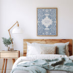 Art print with blue floral patterns and Colossians 1:17 styled above a cozy bed with neutral bedding, a wooden side table, and a minimalist lamp.