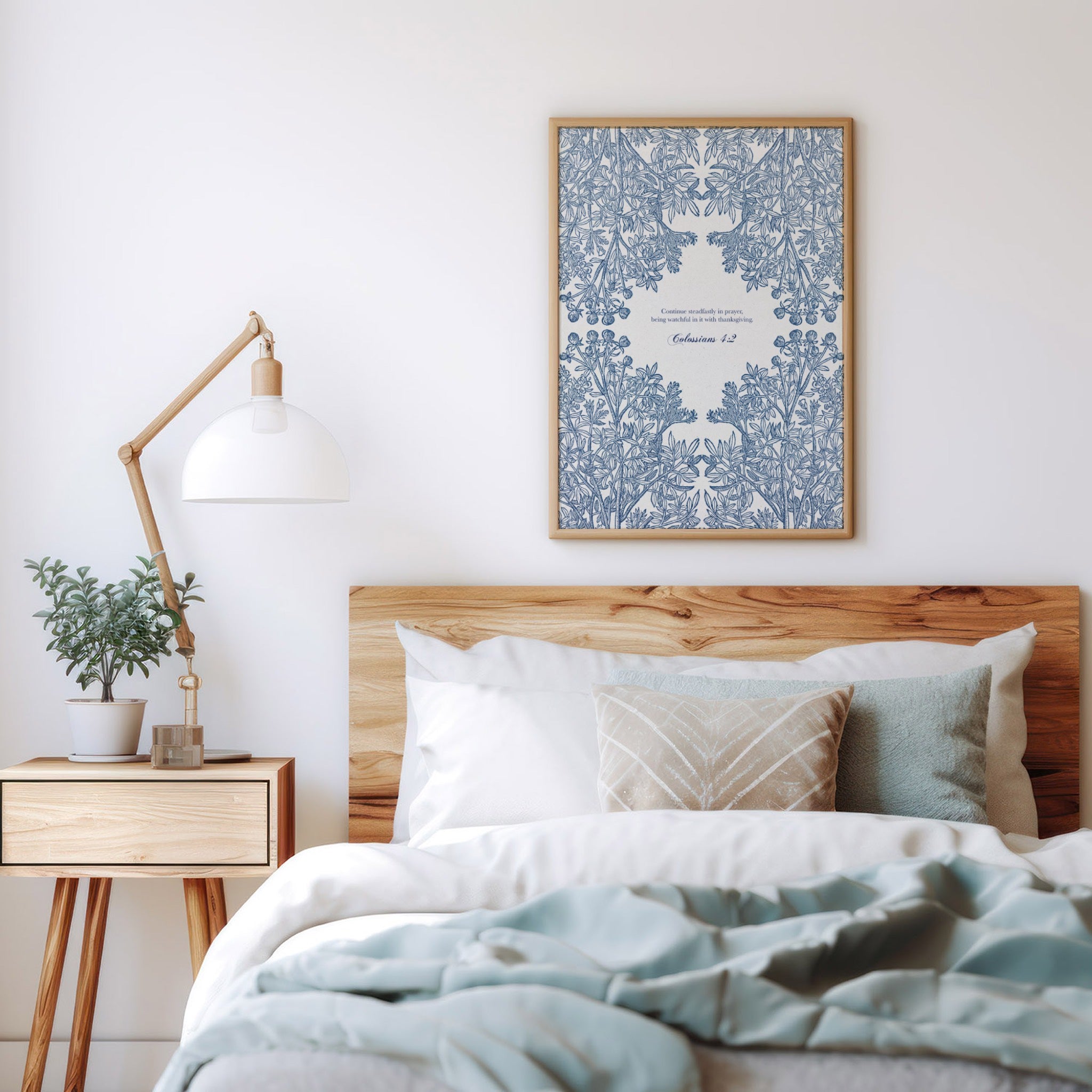 Art print with blue floral patterns and Colossians 1:17 styled above a cozy bed with neutral bedding, a wooden side table, and a minimalist lamp.