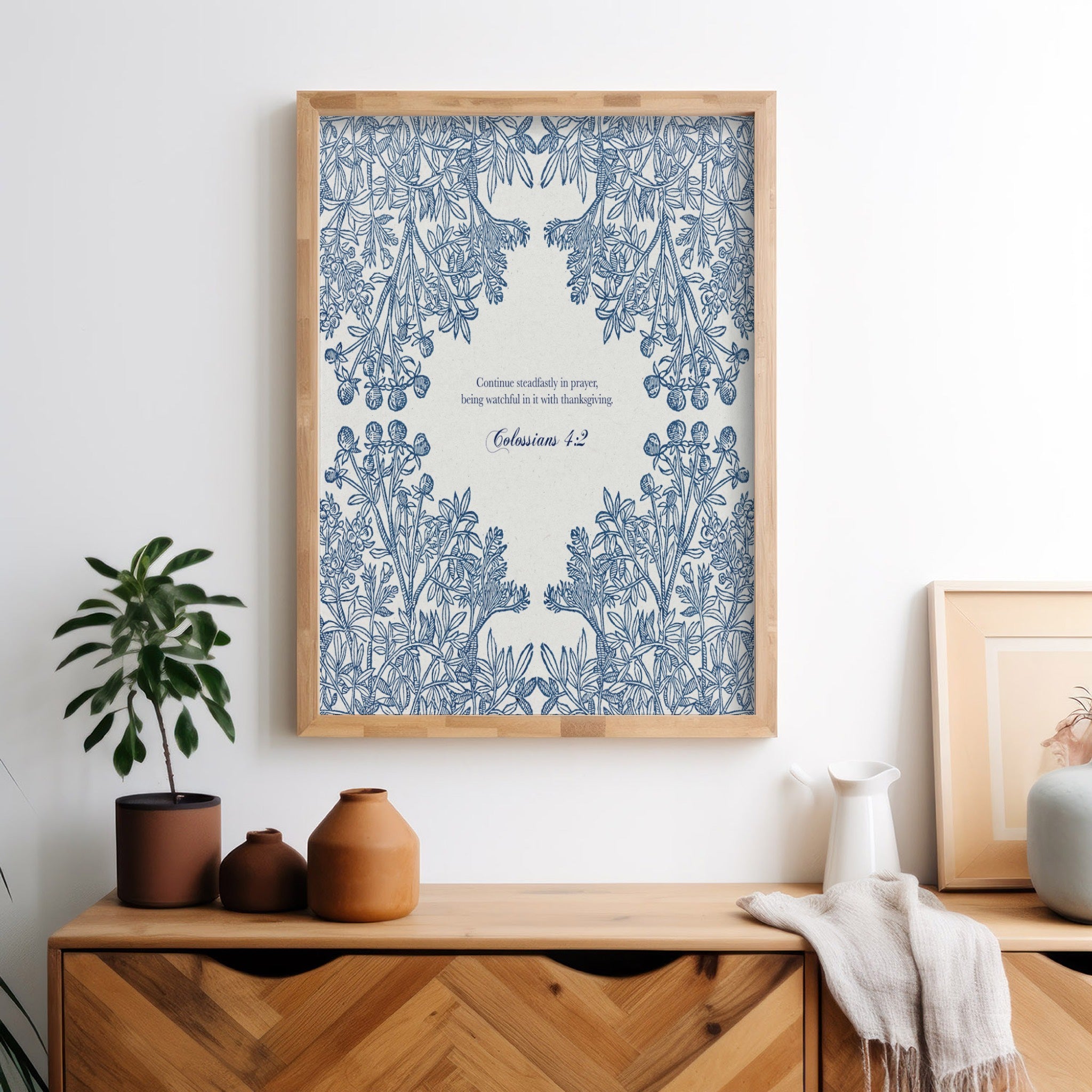 Botanical Bible verse print in blue tones displayed in a modern bedroom setting on a wooden dresser, complemented by a small potted plant and soft decor accents.
