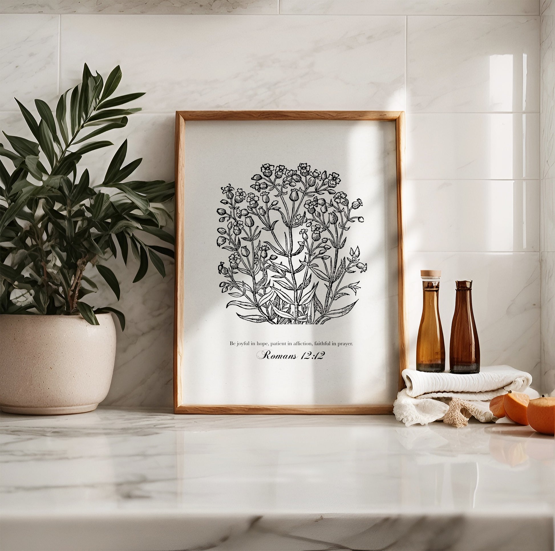 Black floral botanical art print featuring Romans 12:12, styled in a bright kitchen with neutral tones, potted greenery, and amber glass bottles for a serene vibe.