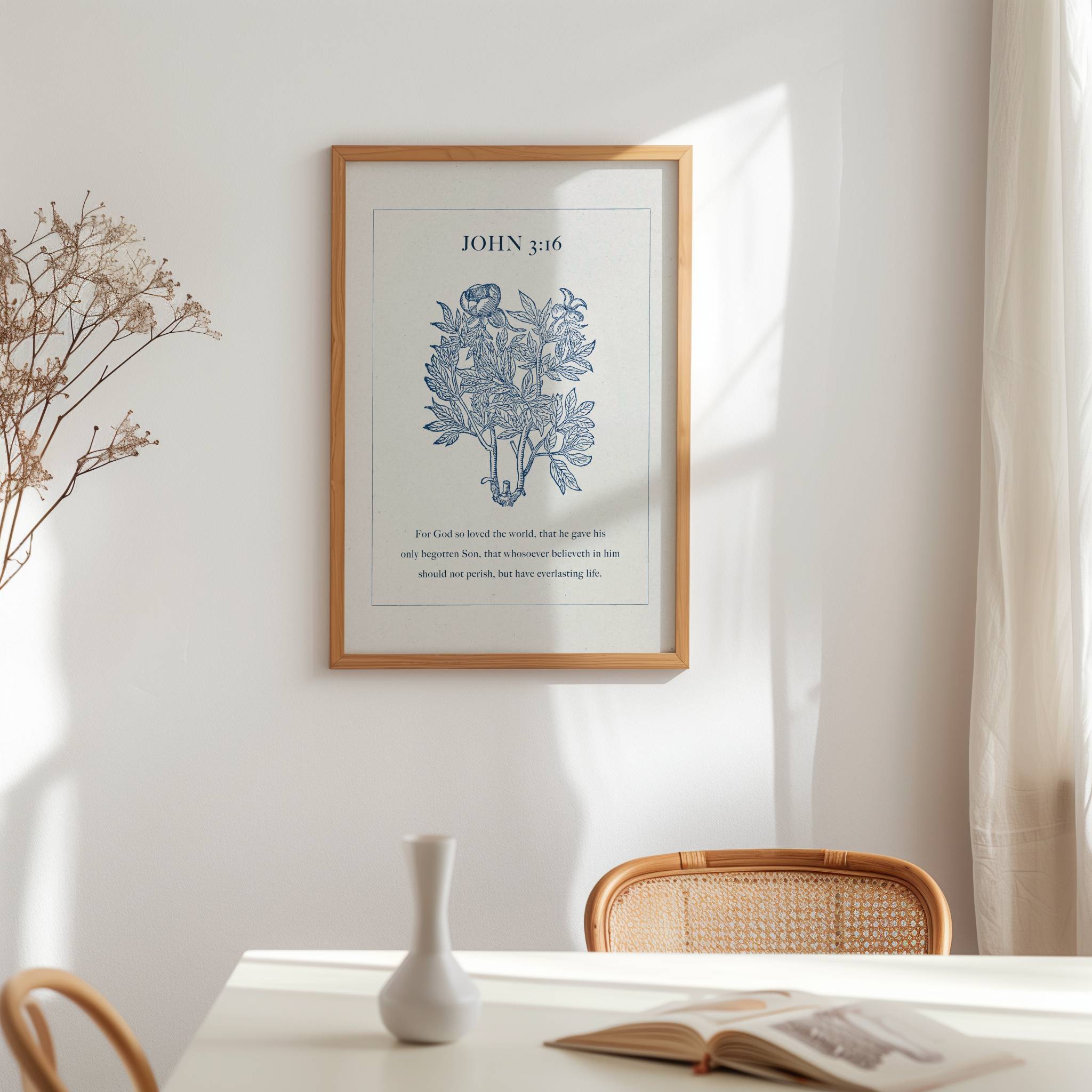 Framed artwork featuring John 3:16 Scripture and blue botanical on a wall above a table with a vase and open book.