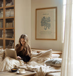 Woman using a laptop on a bed in a cozy room with a bookshelf and framed picture featuring John 3:16 Scripture and blue botanical.